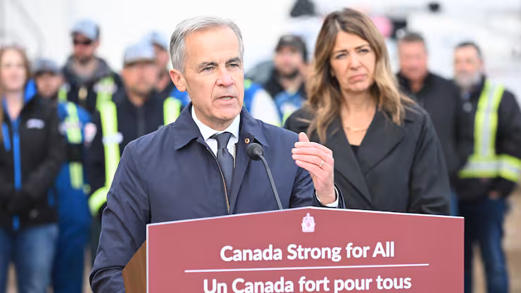Mark Carney prend la parole devant des travailleurs, alors que Danielle Smith se tient derrière lui, lors d’une annonce publique.