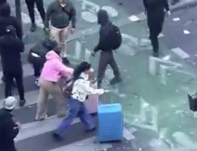 两名身穿粉嫩系服饰的女游客拖著行李箱，在一整群身穿黑衣的抗议人群中显得格外醒目。（X@RafaelSereti）